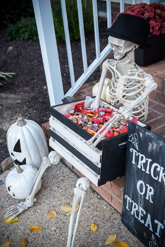 a skeleton sitting on the ground next to a trick or treat box