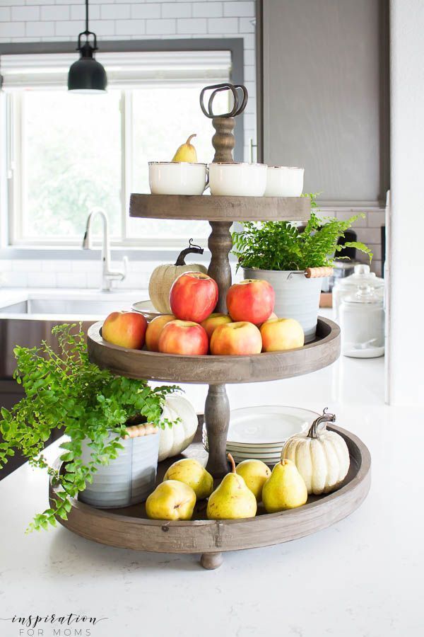 three tiered tray with apples, pears and other fruit on it in a kitchen