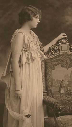 an old photo of a woman standing next to a chair with a painting on it