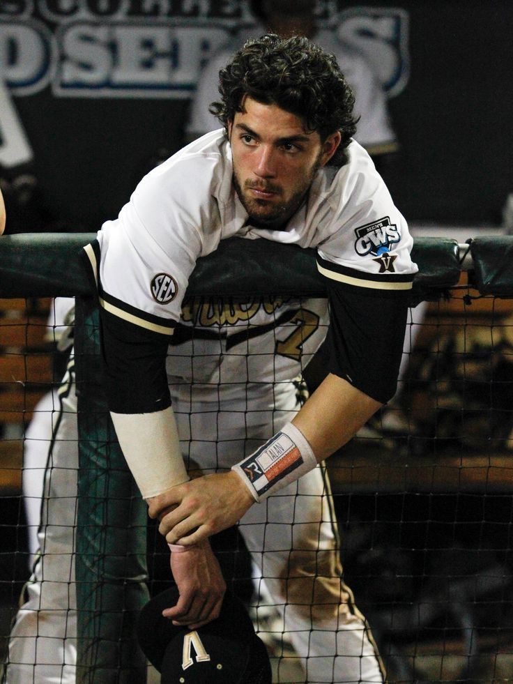 a baseball player leaning on the fence with his glove in his hand and looking down