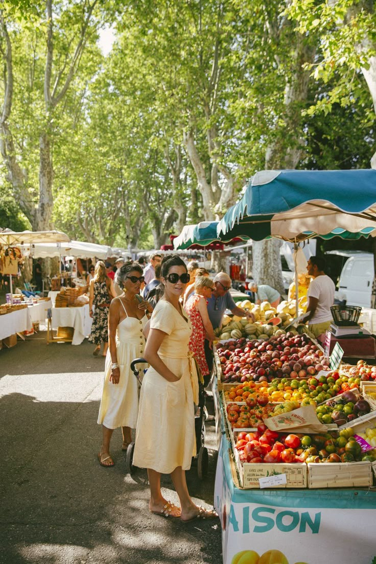 two women are standing in front of a fruit stand at an outdoor farmers'market