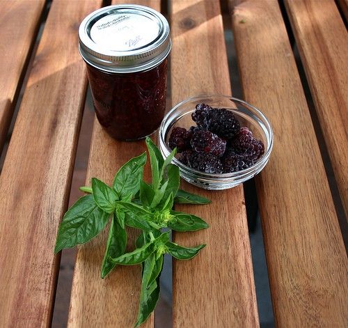 a jar of jam sitting on top of a wooden table next to a bowl of berries