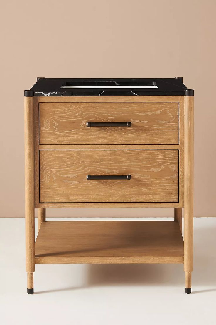 a wooden table with two drawers and a black marble top on the bottom, in front of a beige wall