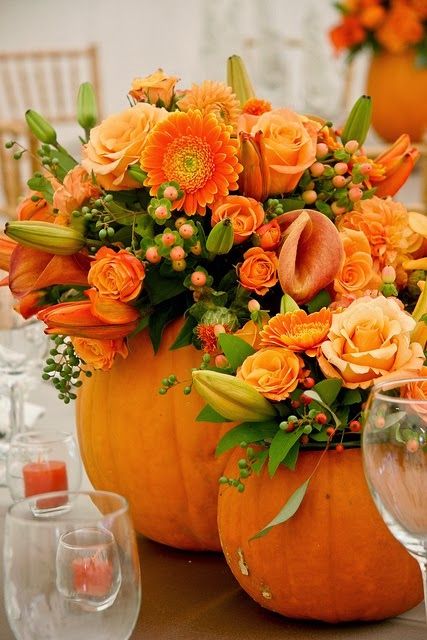 an arrangement of orange flowers and greenery sits in a pumpkin shaped centerpiece on a table