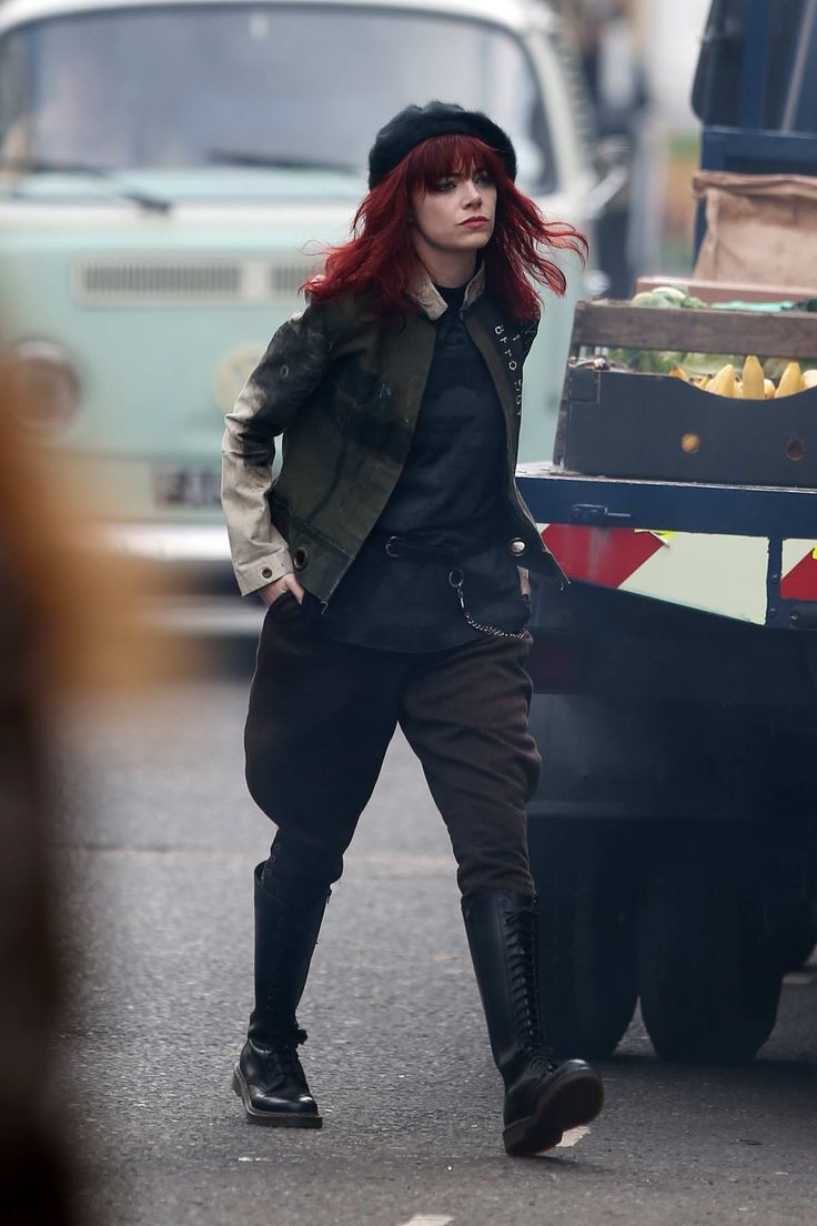 a woman with red hair and black boots walking down the street in front of a truck