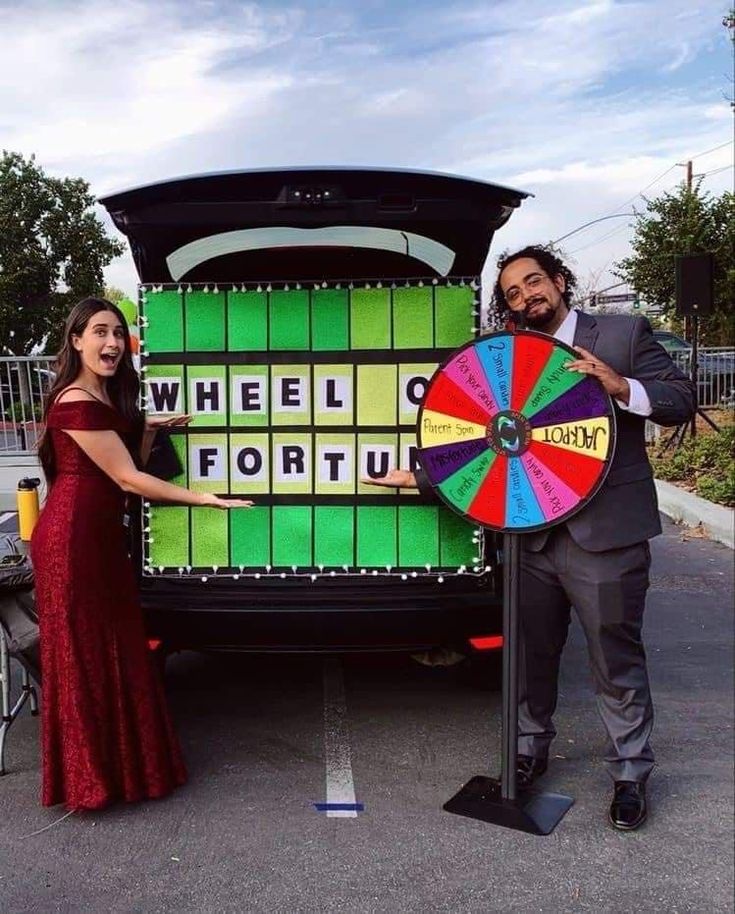 a man and woman standing in front of a wheel of fortune truck with a colorful wheel