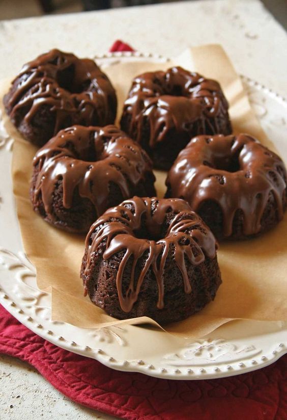 four chocolate donuts on a white plate sitting on a red and white tablecloth