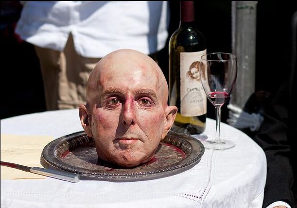 an old man's head sitting on top of a table next to a glass of wine