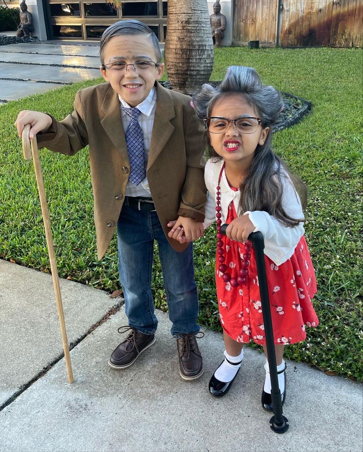 two young children dressed up in costumes and holding canes on the sidewalk, posing for a photo