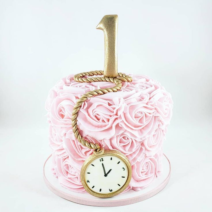 a pink cake decorated with roses and a gold clock for the number one on top