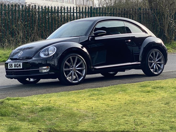 a black car driving down a road next to a lush green field and wooden fence