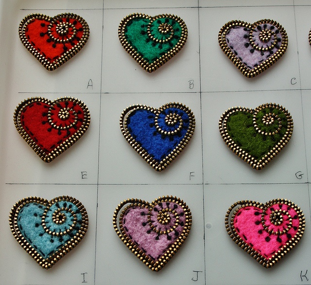 nine heart shaped brooches in various colors and sizes on a white board with black beads