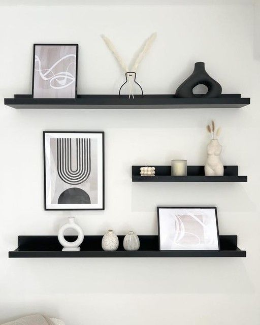 three black shelves with pictures, vases and other items on them in a white room