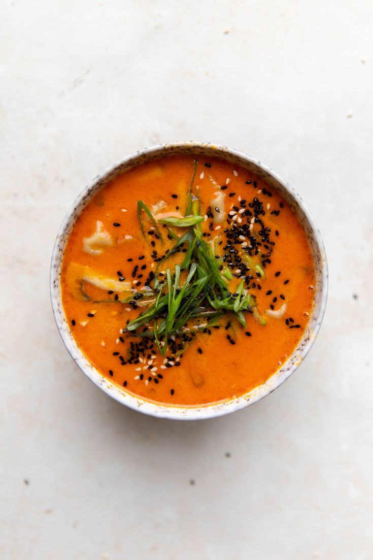 a white bowl filled with carrot soup and topped with black sesame seeds