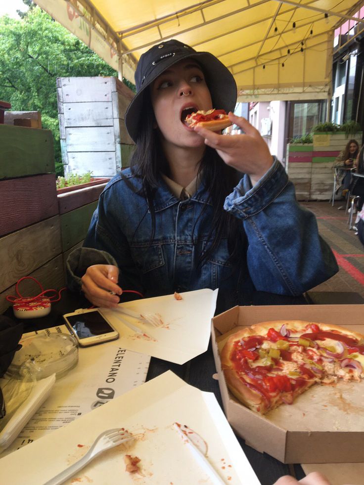 a woman sitting at a table eating a slice of pizza