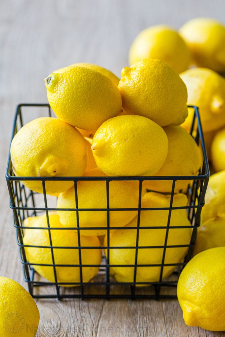 a wire basket filled with lemons sitting on top of a wooden table next to other lemons