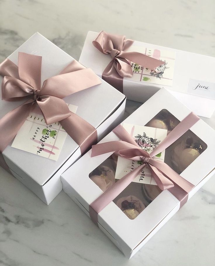 three white boxes with pink bows on top of each one and two pictures in the middle