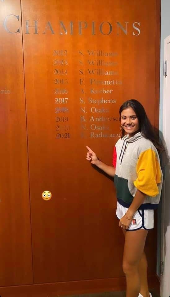 a woman standing in front of a wall with the names of tennis players on it