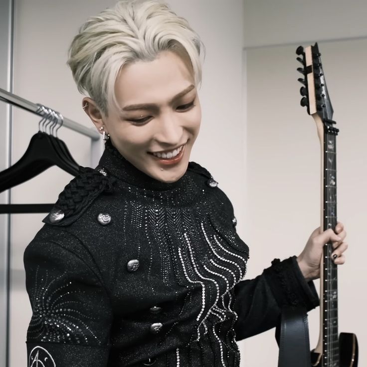 a woman holding a guitar in her right hand and smiling while standing next to a rack with guitars on it