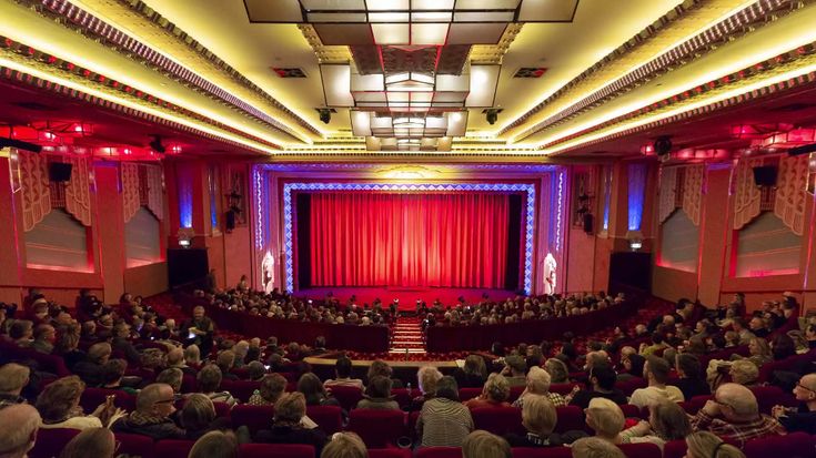 an auditorium filled with people and red curtains