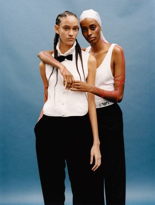 two women standing next to each other with their arms around one another, both wearing white shirts and black pants