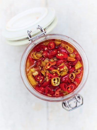 a glass bowl filled with red and yellow bell peppers next to a white plate on a table