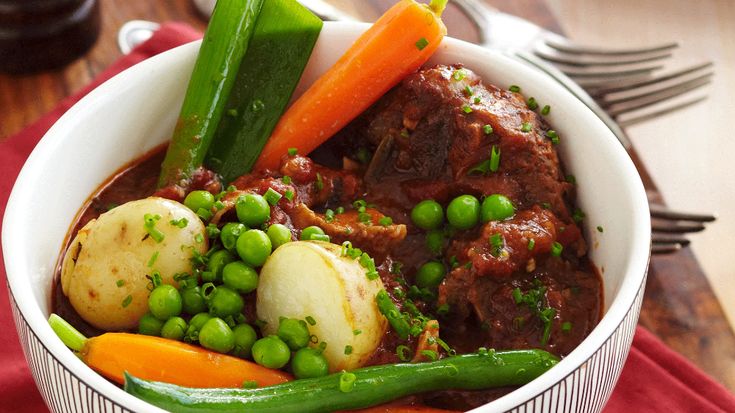 a bowl filled with meat and vegetables on top of a red cloth next to silverware