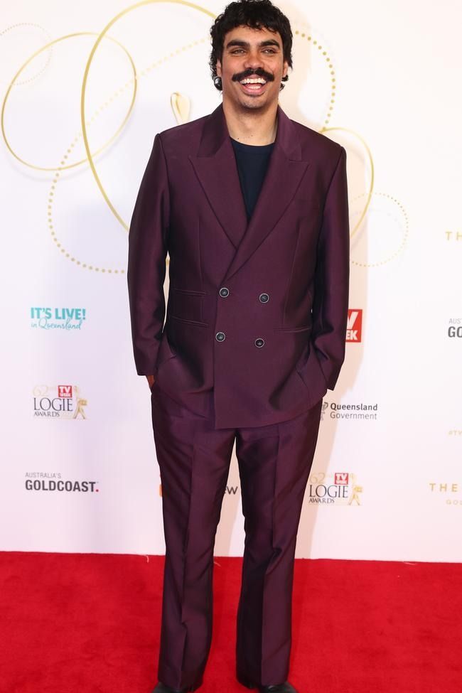 a man in a purple suit standing on a red carpet