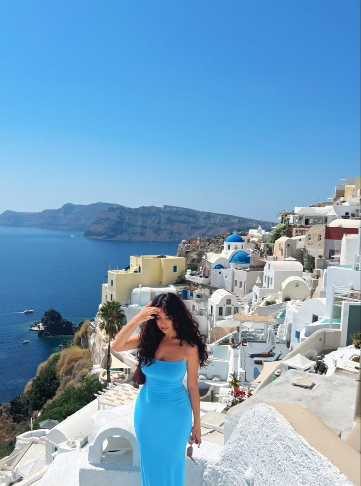 a woman in a blue dress standing on the edge of a cliff looking at the ocean