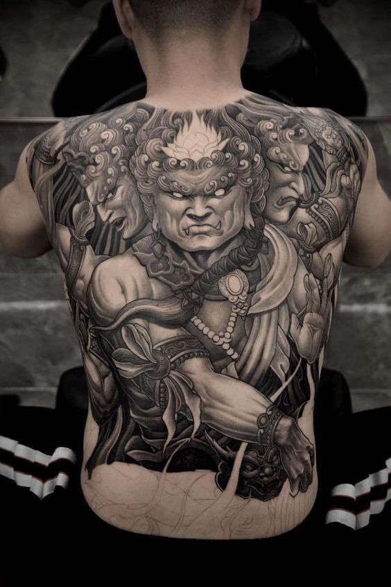 the back of a man's body with tattoos on it and an image of a demon