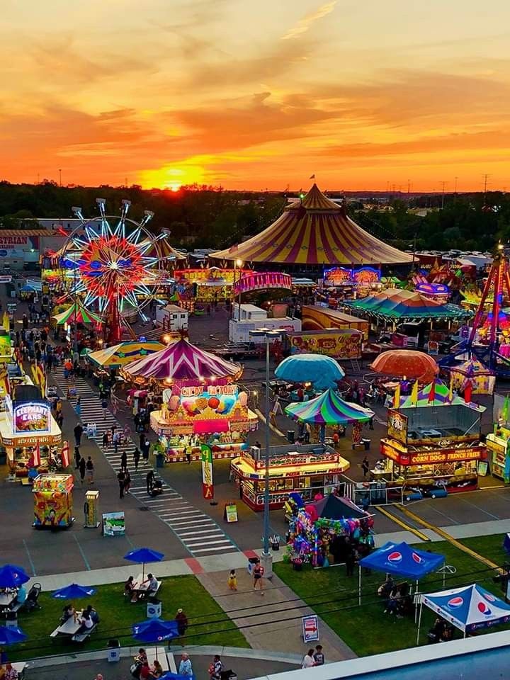 an aerial view of the fairground at sunset or dawn, with many rides and carnival booths