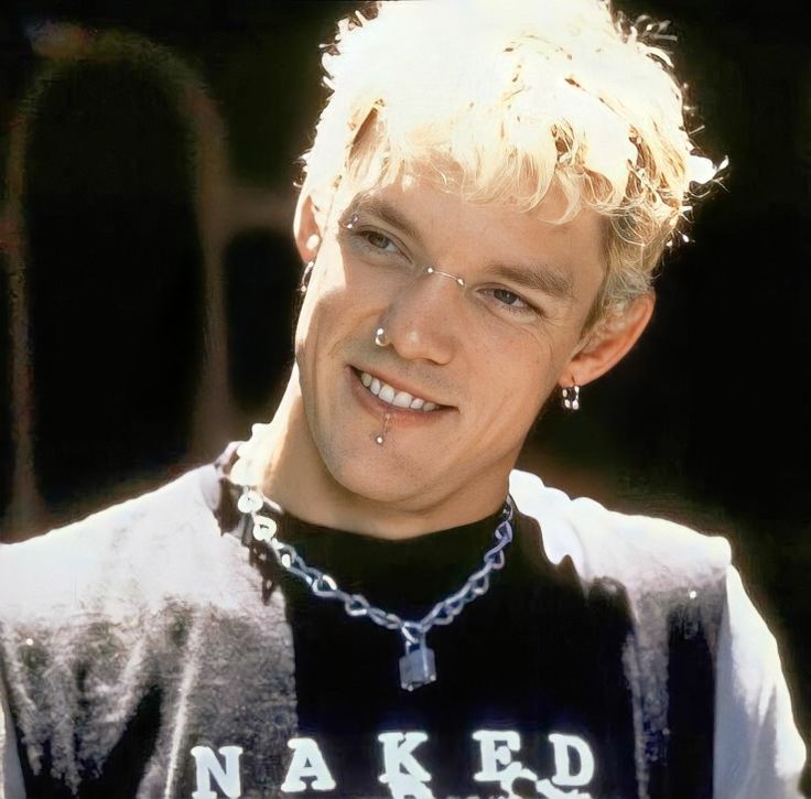 a young man with blonde hair wearing a black shirt and silver chain around his neck