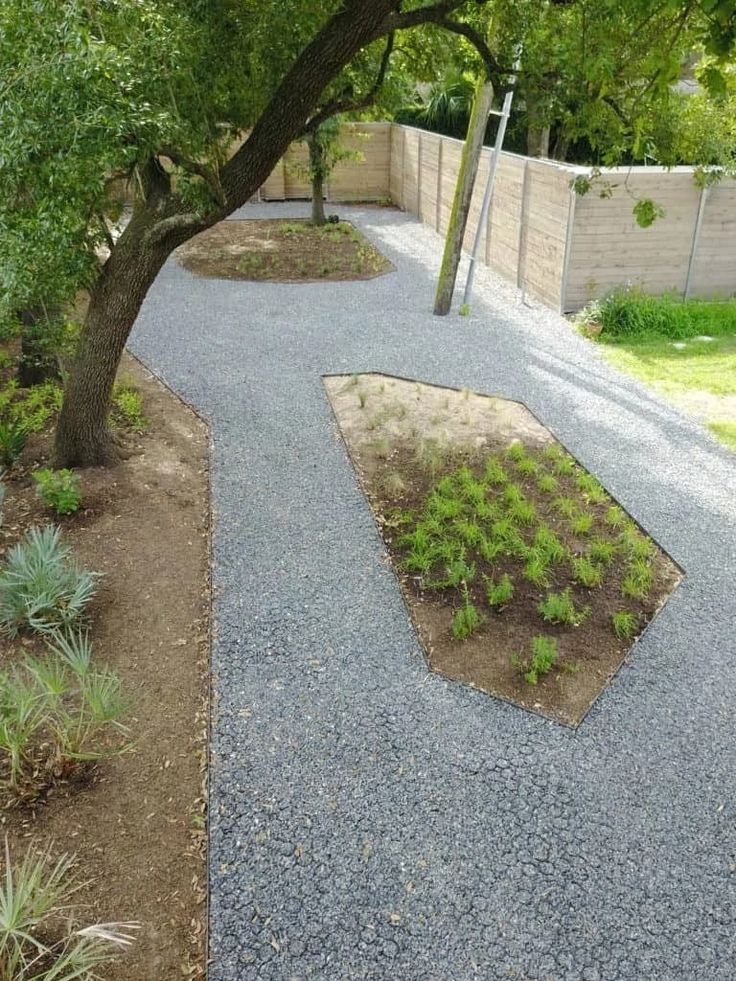 a gravel path in the middle of a garden with trees and plants on both sides