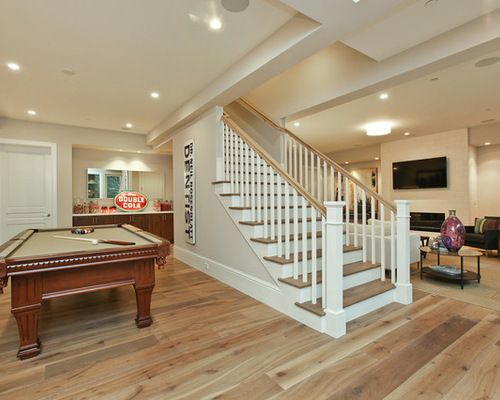 a pool table in the middle of a living room with stairs leading up to it