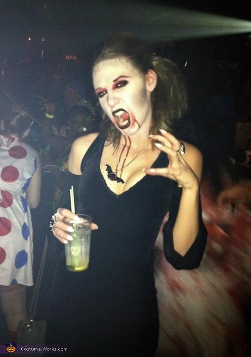 a woman dressed up as a zombie holding a drink in her hand and making a weird face