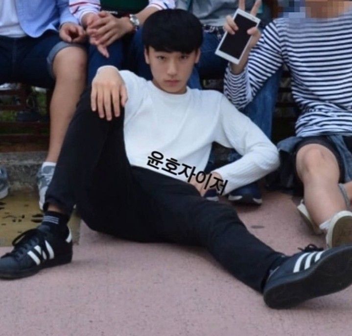 a young man sitting on the ground with his legs crossed in front of him and two other people behind him