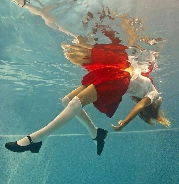 a woman in red skirt and white shirt under water with her feet on the ground