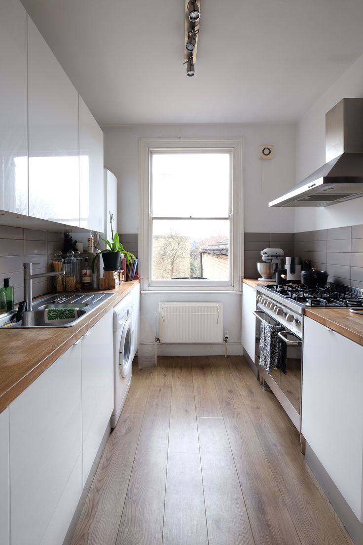 a kitchen with wooden floors and white cabinets, an oven, dishwasher, sink and window