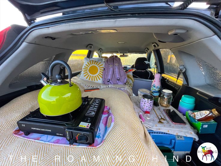 the trunk of a car with various items in it, including a tea kettle and books