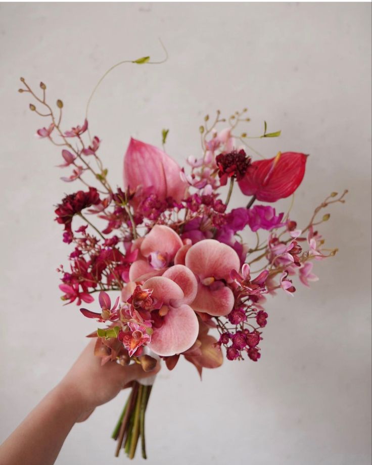 a person holding a bouquet of flowers in their hand with pink and red flowers on it