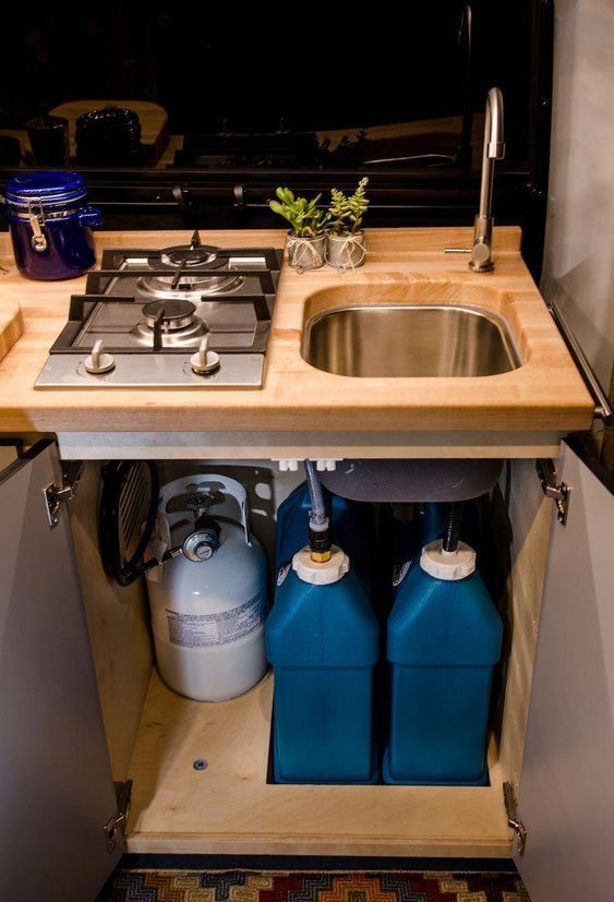 a kitchen sink with two blue containers under it and a stove top oven next to it