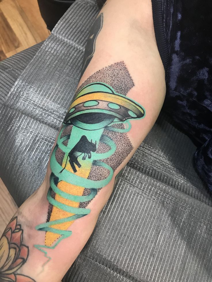 a person with a tattoo on their arm wearing a green hat and an alien flying saucer