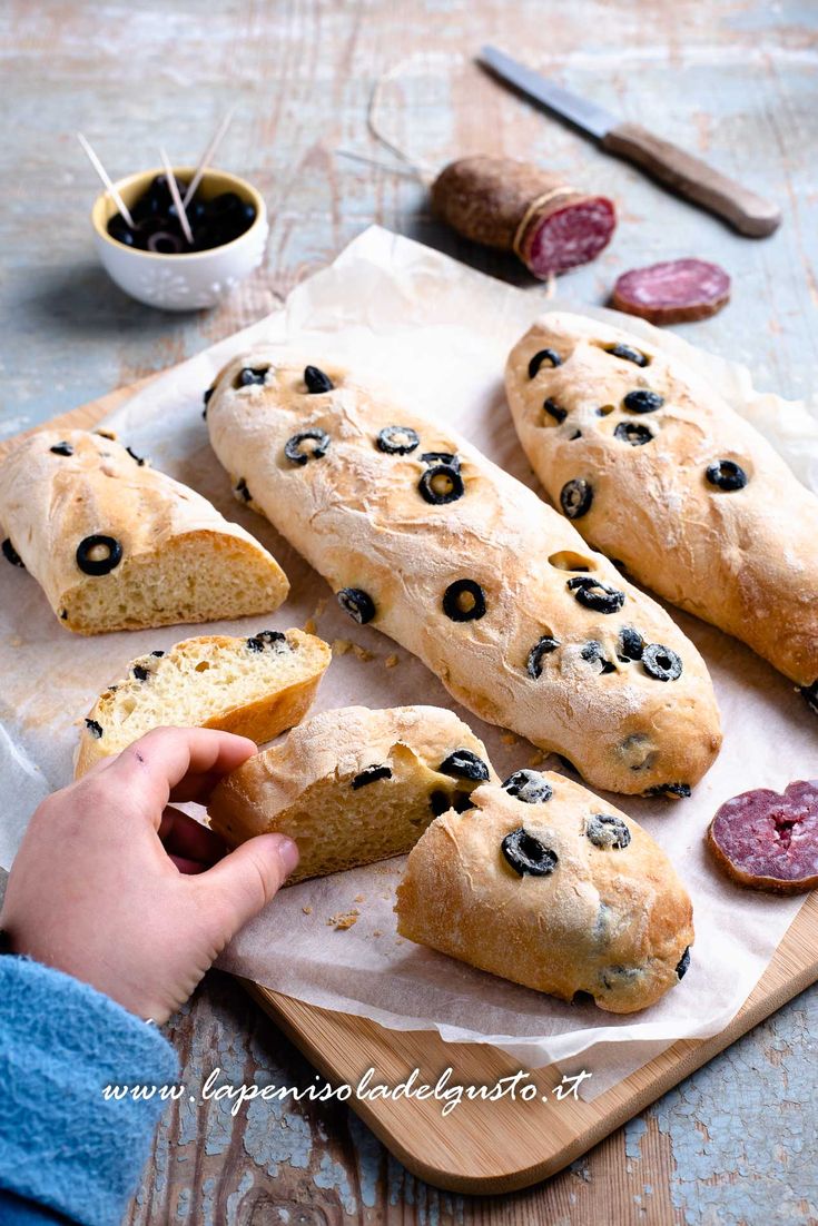 a person holding a piece of bread with olives on it next to other food items