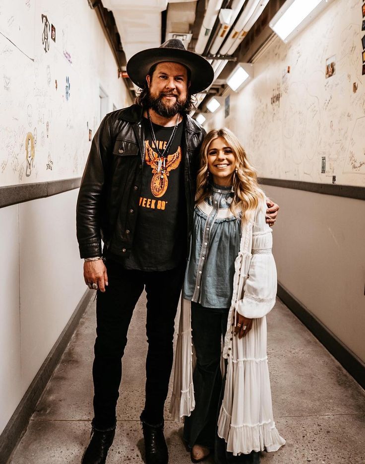 a man standing next to a woman wearing a cowboy hat in a hallway with white walls