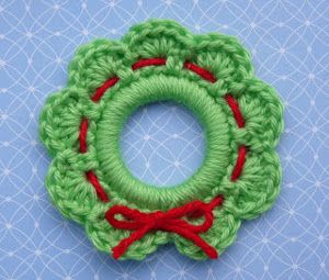 a green crocheted brooch with red ribbon around it on a blue background