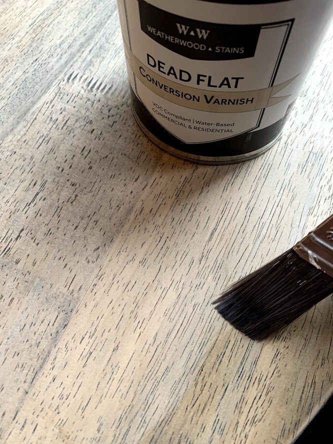 a paint can sitting on top of a wooden table with a brush next to it