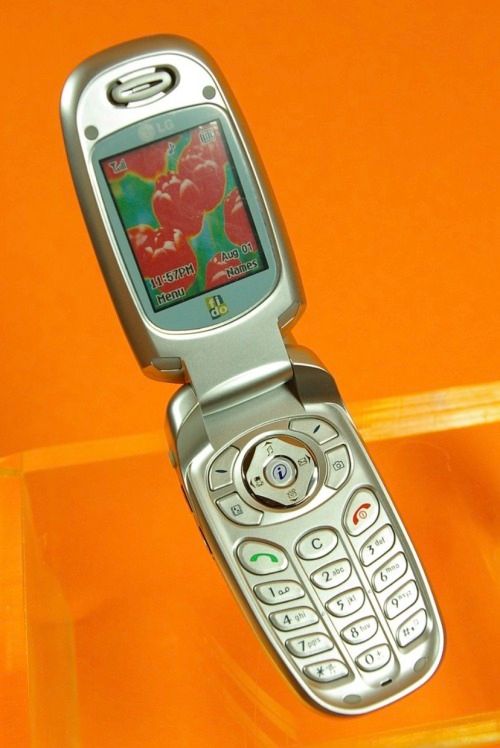 an old cell phone sitting on top of a glass table next to a yellow wall