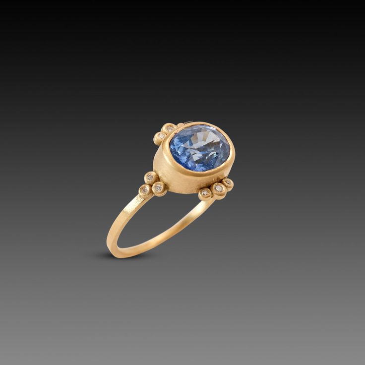 This stunning ring features a vibrant oval shaped blue sapphire, framed by twelve sparkling white diamonds. This very special gem is set in 18k yellow gold on a 1.5mm band. The center stone measures 7mm x 9mm, and weighs 3.59 ct. Matte finish. Modern Sapphire Ring With Rose Cut Diamonds, Yellow Gold Sapphire Ring With Diamond Oval Cabochon, Yellow Gold Sapphire Diamond Ring With Oval Cabochon, Oval Cabochon Sapphire Ring In Yellow Gold With Diamond, Oval Cabochon Sapphire Rings In Yellow Gold, Oval Sapphire Rings With Single Cut Diamonds, 14k Gold Sapphire Ring With Rose Cut Diamonds, Oval Sapphire Diamond Ring With Single Cut Diamonds, Oval Yellow Gold Sapphire Ring With Single Cut Diamonds