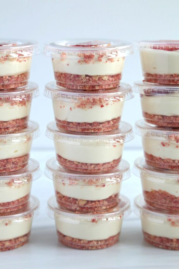 there are many desserts in plastic containers stacked on top of each other with white frosting and red sprinkles