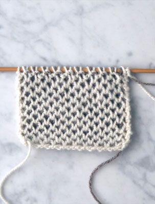 a close up of a knitted bag on a marble surface with a knitting needle